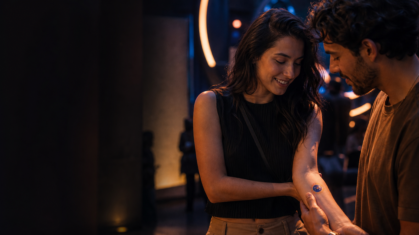Dos asistentes observan un tatuaje temporal circular aplicado en un antebrazo durante una activación nocturna