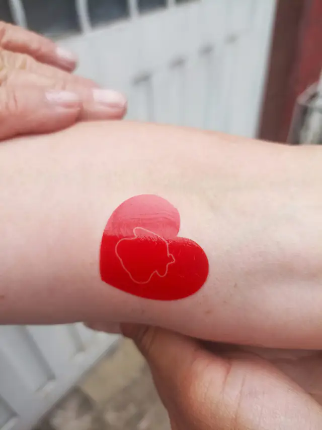 Tatuaje temporal de corazón rojo con la silueta de una casa, aplicado en el brazo para Davivienda